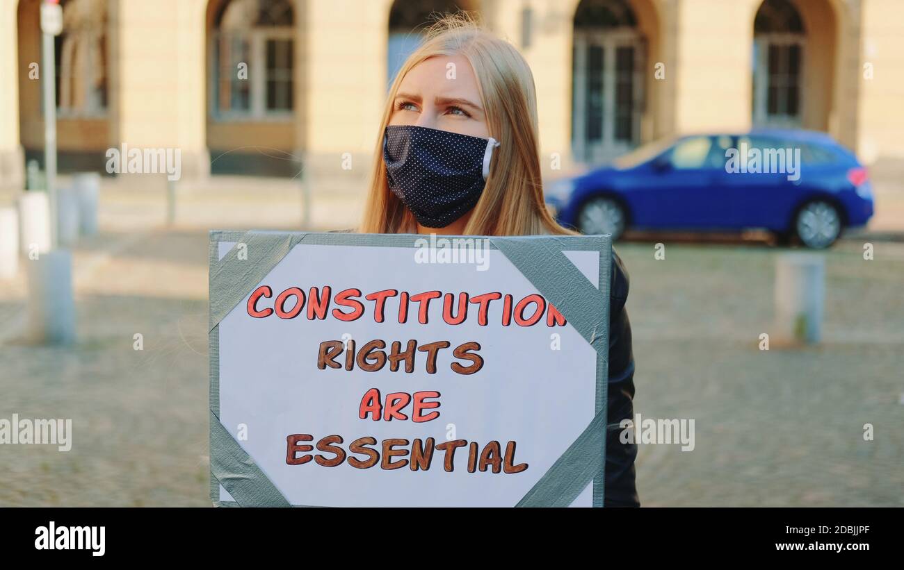 Protesta a piedi: Donna in maschera protettiva che sostiene per la protezione dei diritti costituzionali. Tiene la bandiera e va sulla strada. Foto Stock
