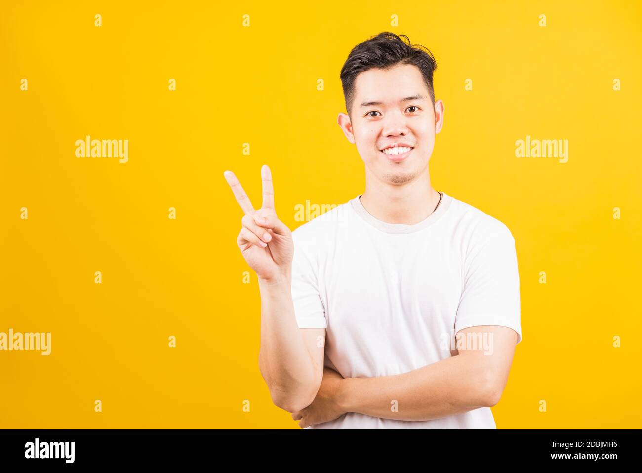 Ritratto felice asiatico bel giovane uomo sorridente in piedi indossando una t-shirt bianca che mostra le dita facendo vittoria V segno o numero due, guardando a cammello Foto Stock