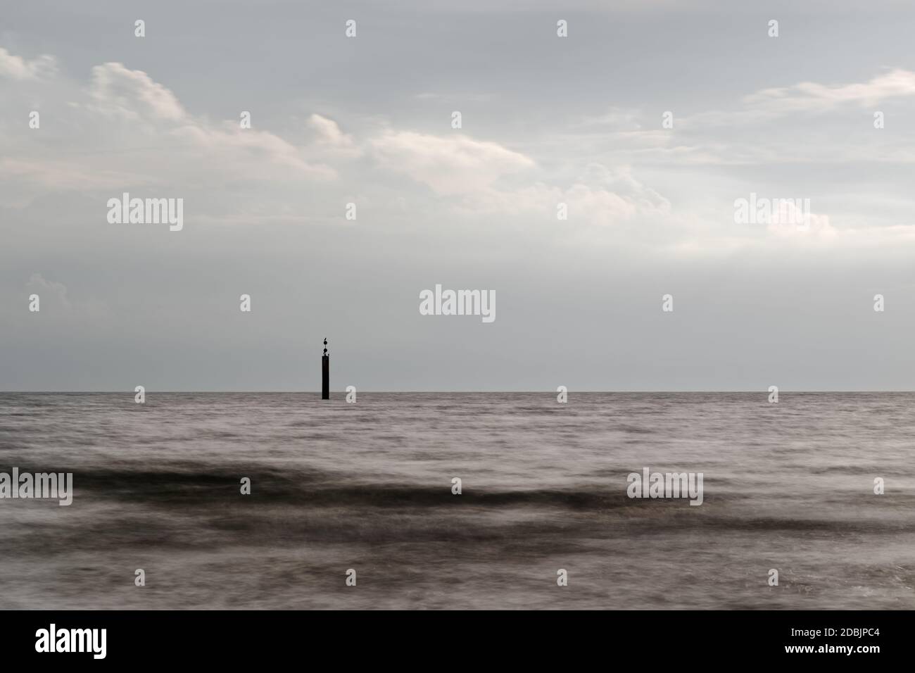 Tranquilla spiaggia ripresa della costa del Mar Baltico con una prominente struttura ad onda e un palo di segnale sullo sfondo, la superficie dell'acqua è levigata da ti lungo Foto Stock