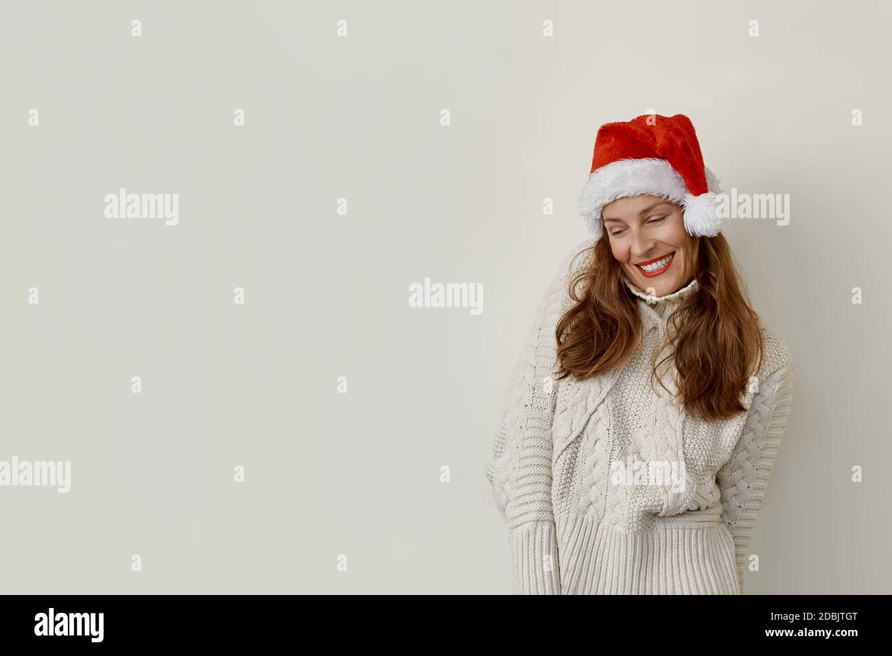 Donna che indossa un maglione e un cappello di santa che guarda verso il basso e sorridendo Foto Stock