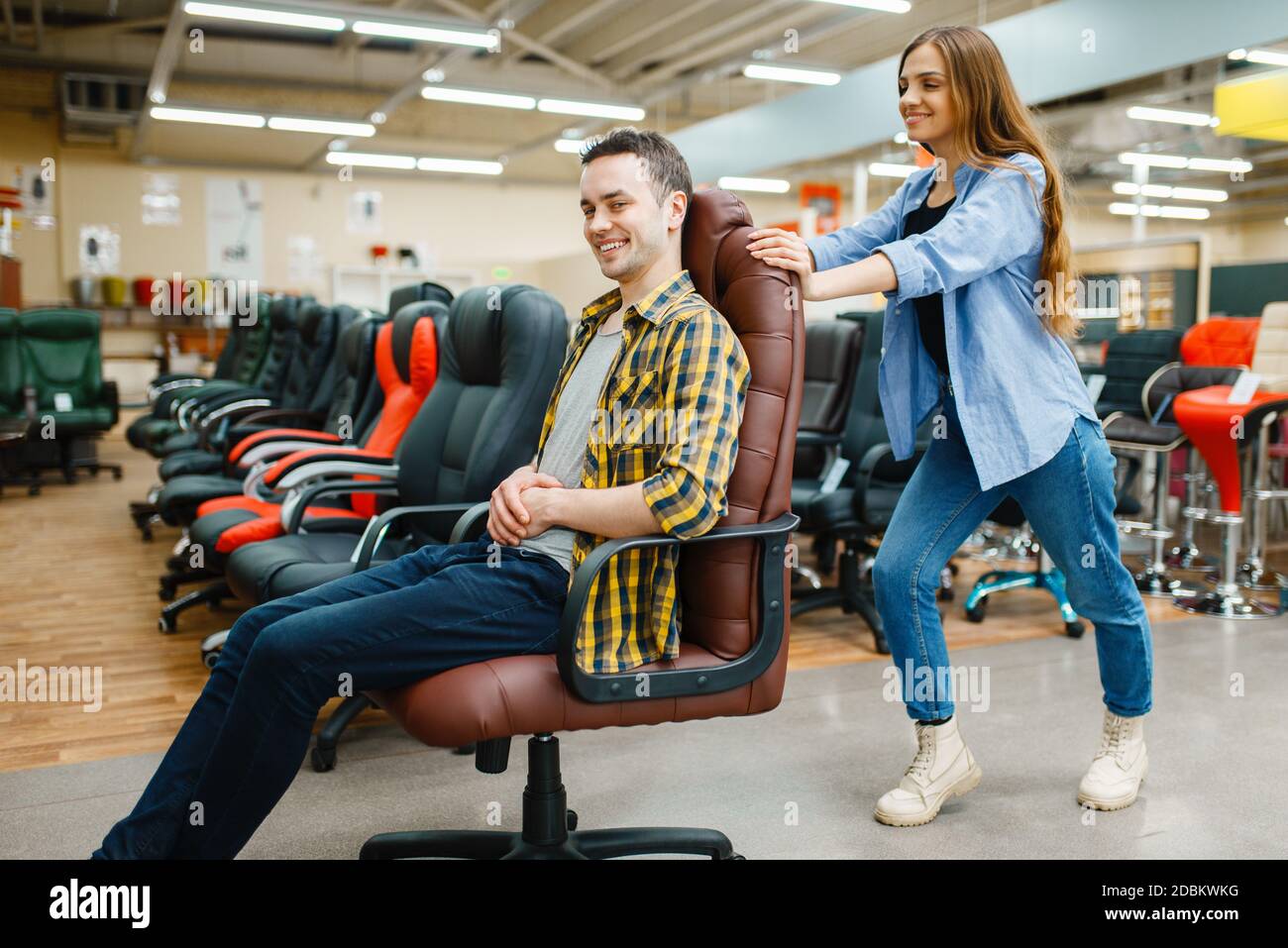 Happy giovane coppia ride sulla sedia da ufficio nello showroom del negozio  di mobili. Uomo e donna in cerca di campioni per la camera da letto in  negozio, marito e moglie compra