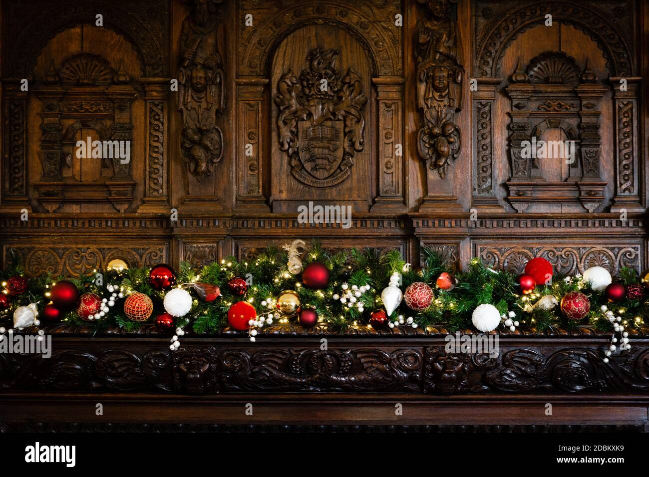 Un bel fuoco di legno tradizionale circondato da intricati intagli adornati con un festoso Natale ghirlanda di rosso, verde e oro. Foto Stock