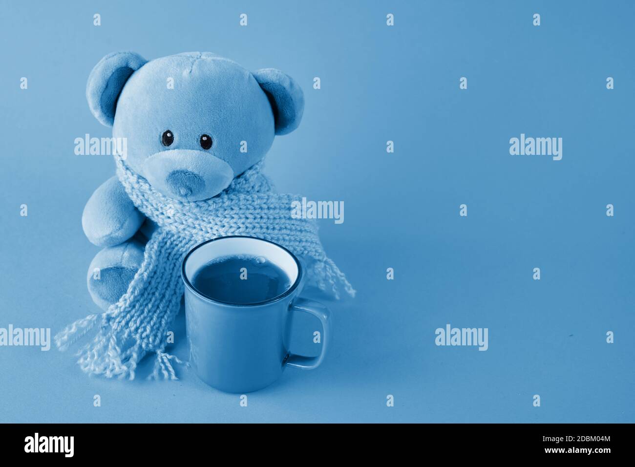 Orsacchiotto blu con sciarpa e tazza di caffè su sfondo blu. Concetto di lunedì blu. Foto Stock