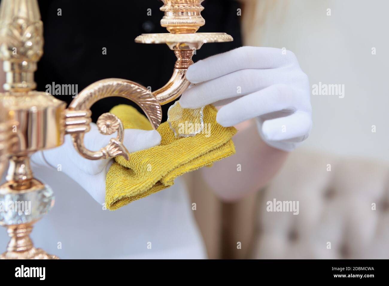 Le mani da donna in guanti di cotone bianco strofinano i pendenti in vetro della piantana. Pulizia delle camere d'albergo. Il concetto di pulizia e ordine nella r Foto Stock