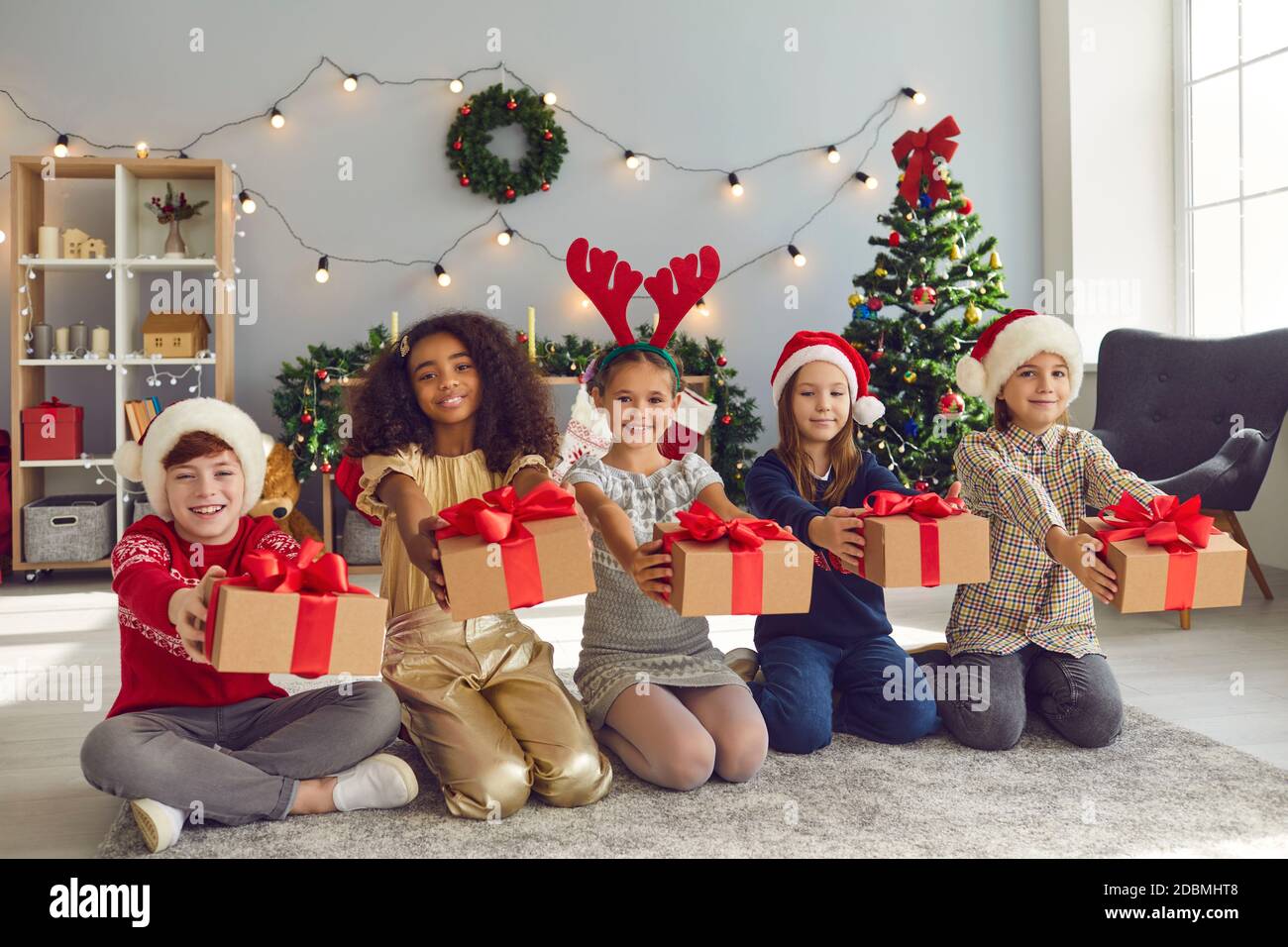 Gruppo di bambini felici e diversi seduti sul pavimento e. Regali di Natale Foto Stock