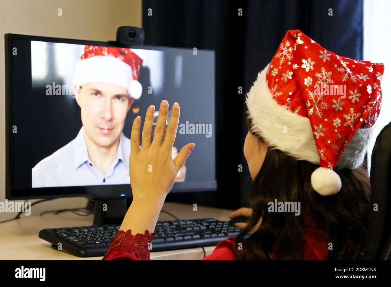Festa di Capodanno a distanza durante la pandemia del coronavirus. Donna in cappello di Santa seduta davanti alla webcam del PC Foto Stock