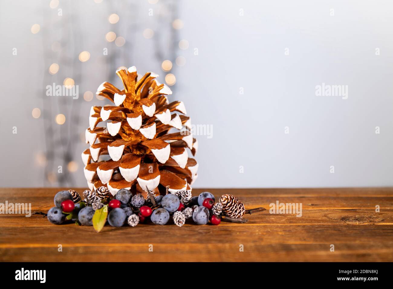 Brillante atmosfera natalizia con materiali naturali: oro e bianco dipinto a mano pinecone impreziosito da bacche blu e rosso disposti sul tavolo Foto Stock