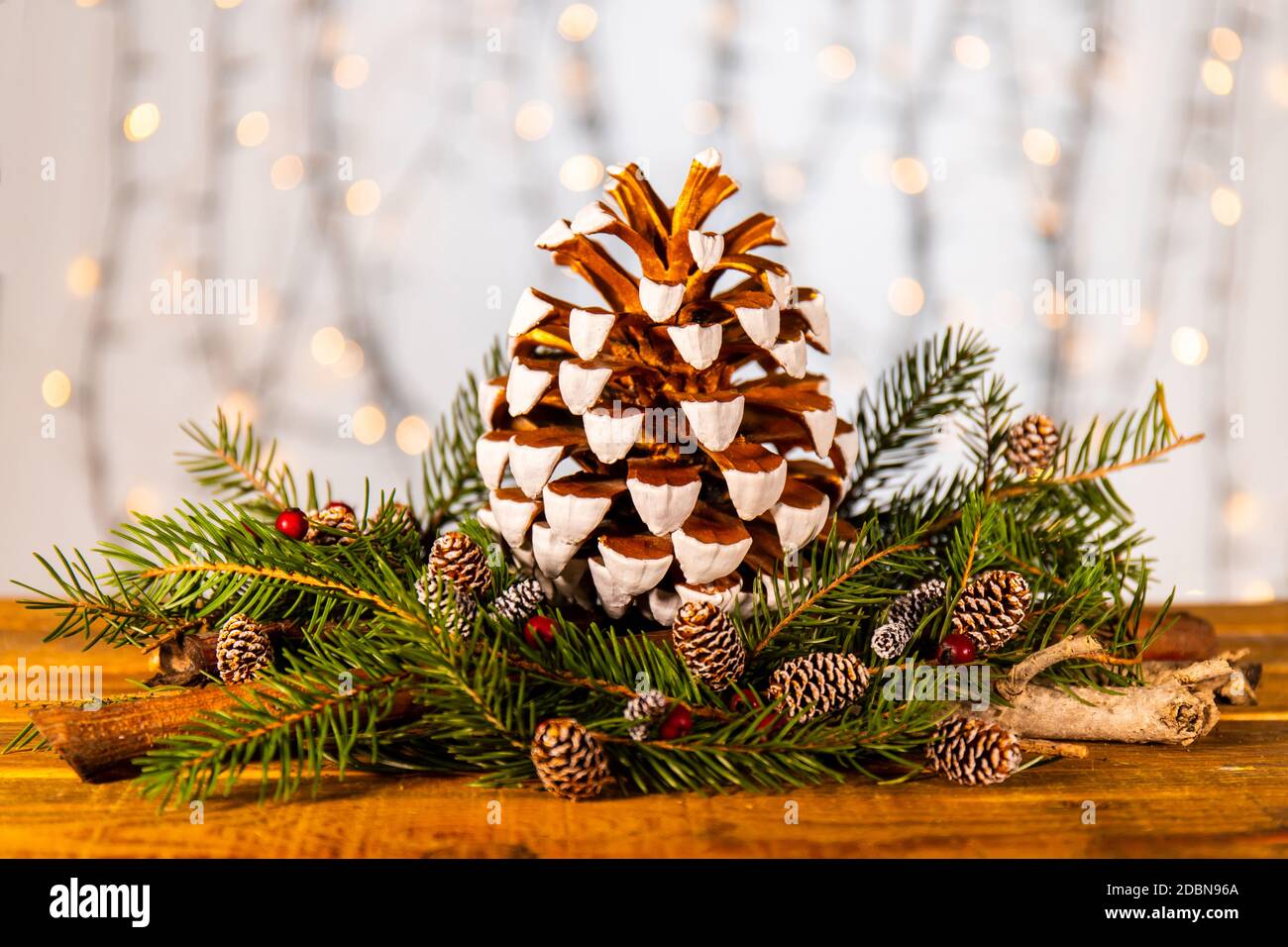 Ornamento di xmas pinecone. pinecone dipinto in bianco e oro impreziosito da rami di abete verde e base di frutti rossi. Foto Stock