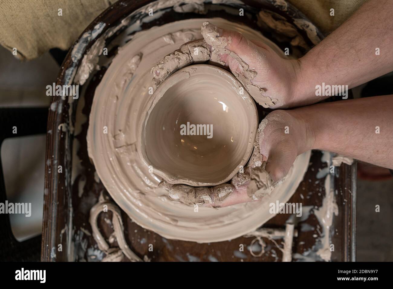 Primo piano di una mano di Potter scolpisce un caraffa di creta su una ruota di Potter Foto Stock