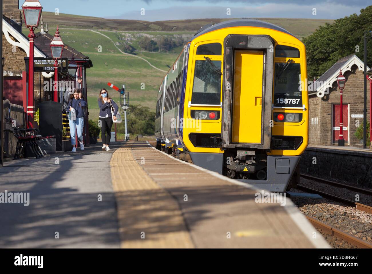 Il passeggero indossa una maschera facciale che lascia una classe Northern Rail 158 Sprinter alla stazione ferroviaria di Garsdale Foto Stock