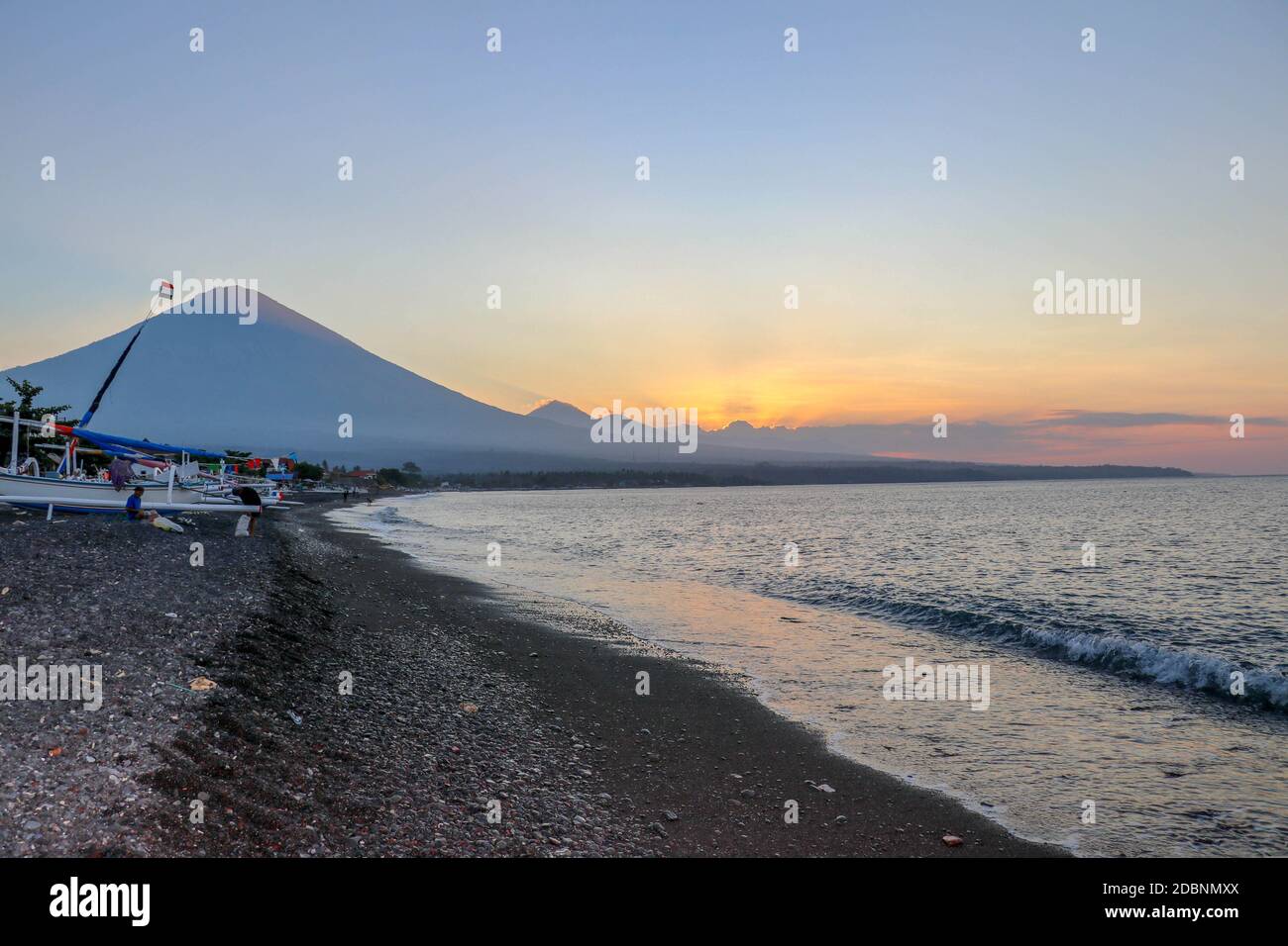 Tramonto sulla spiaggia su un isola tropicale. Colore arancio Cielo e nubi. Grande maestoso vulcano all'orizzonte. Mare tranquilla e romantica atmosfera. Foto Stock