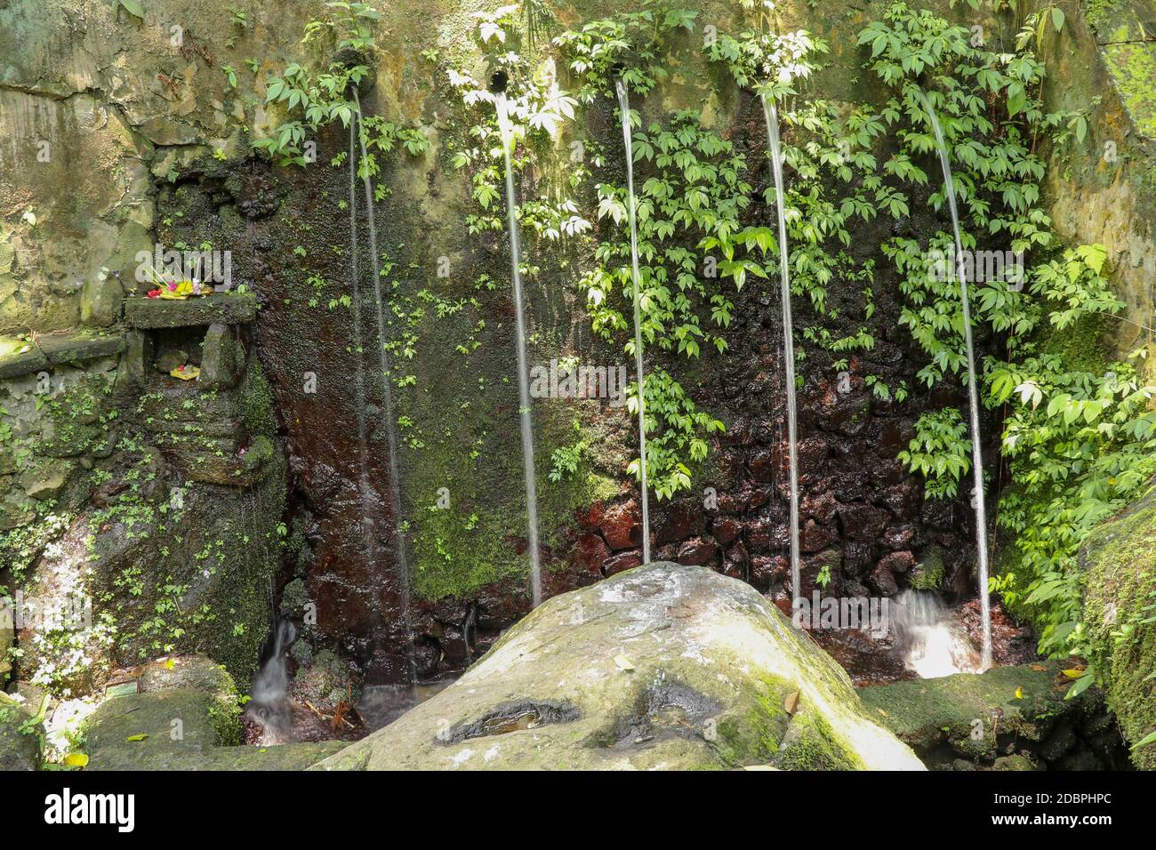 Sorgenti d'acqua sacra nella Valle Pakerisan presso il complesso di sepoltura di Tampaksiring. Gunung Kawi, Bali, Indonesia. Sacrifici agli dei sull'altare. Io Foto Stock