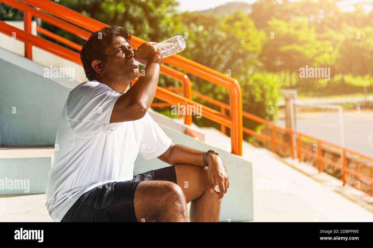 runner uomo nero indossa le cuffie dell'atleta che beve acqua Foto Stock