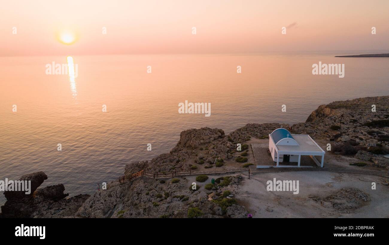 Vista aerea del tramonto della costa e simbolo bianco cappella Agioi Anargyroi, a cavo Greco Protaras, Famagosta, Cipro dall'alto. Vie dell'occhio dell'uccello Foto Stock