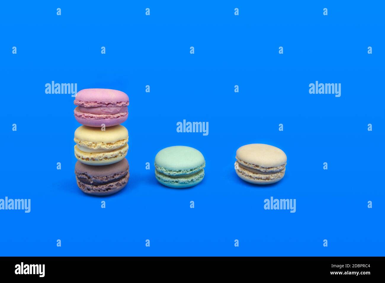 Immagine di alcuni macaron di vari colori, impilati su un tavolo e sfondo blu, con spazio per la copia Foto Stock