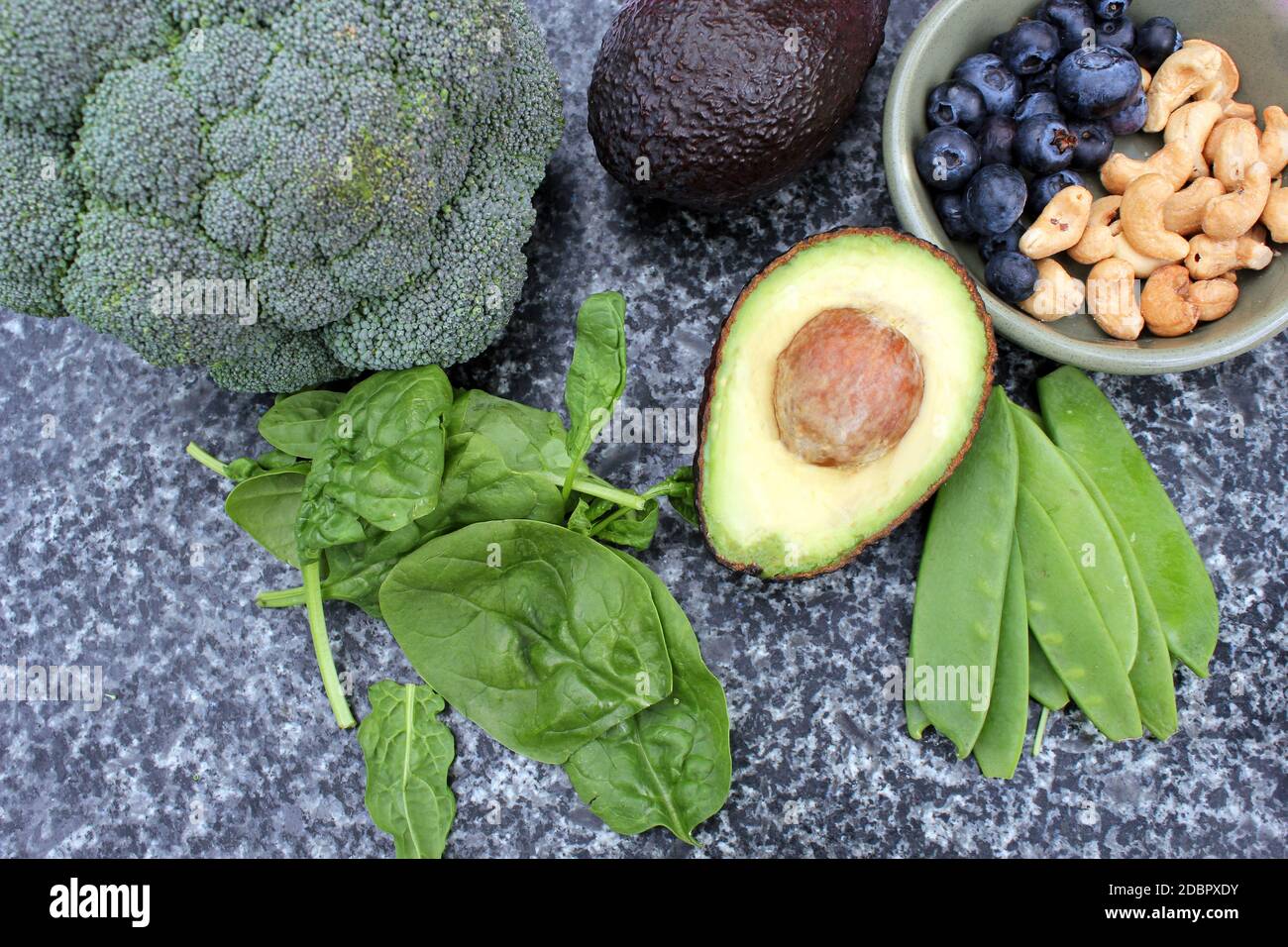 Dieta vegetariana vegana a base di piante selezione senza glutine di noci di anacardi, mirtilli, spinaci, piselli da mange e tois avocado e broccoli su sfondo di marmo e tavola Foto Stock