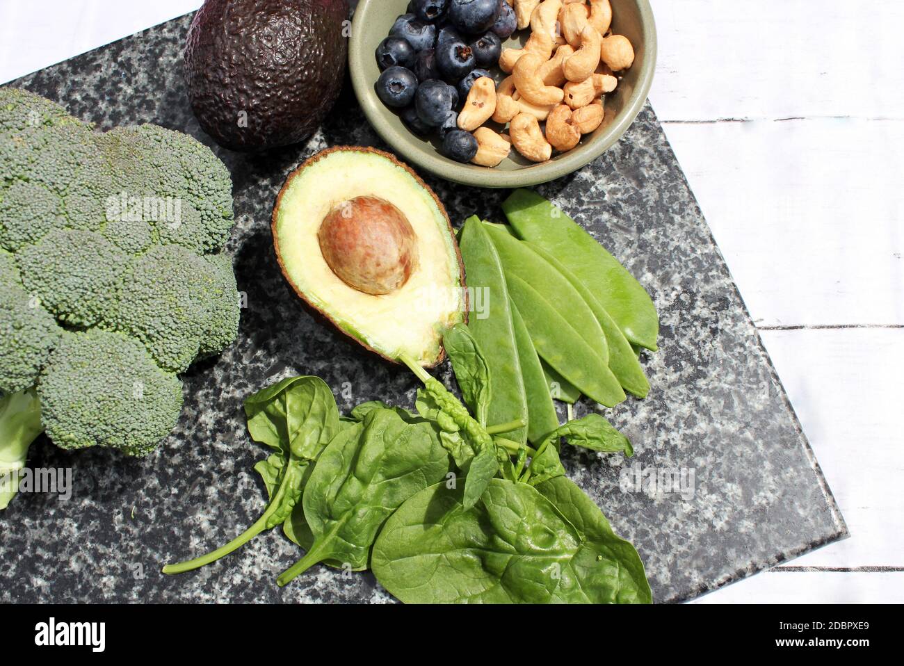 Dieta vegetariana vegana a base di piante selezione senza glutine di noci di anacardi, mirtilli, spinaci, piselli da mange e tois avocado e broccoli su sfondo di marmo e tavola Foto Stock