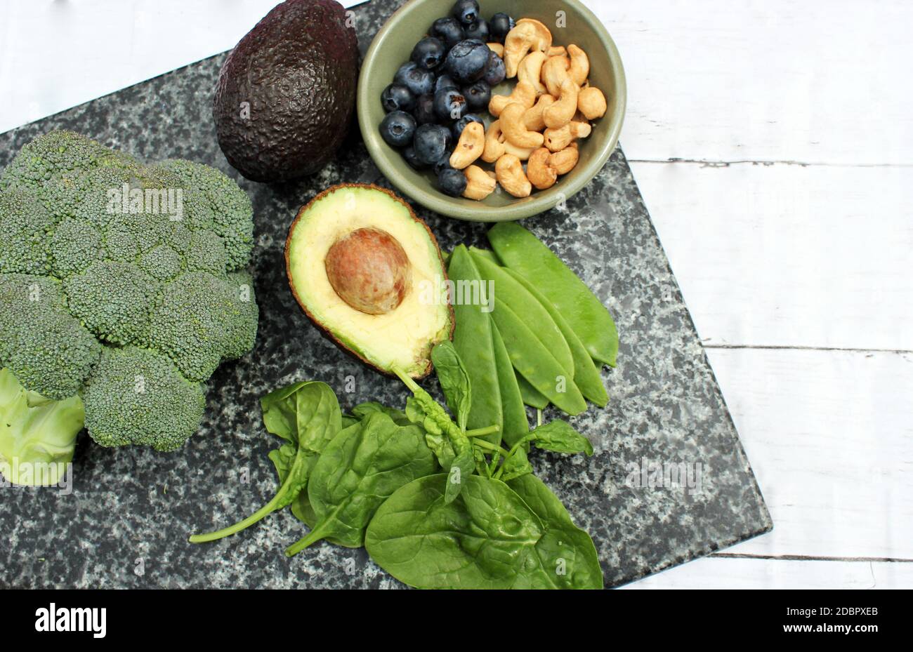 Dieta vegetariana vegana a base di piante selezione senza glutine di noci di anacardi, mirtilli, spinaci, piselli da mange e tois avocado e broccoli su sfondo di marmo e tavola Foto Stock