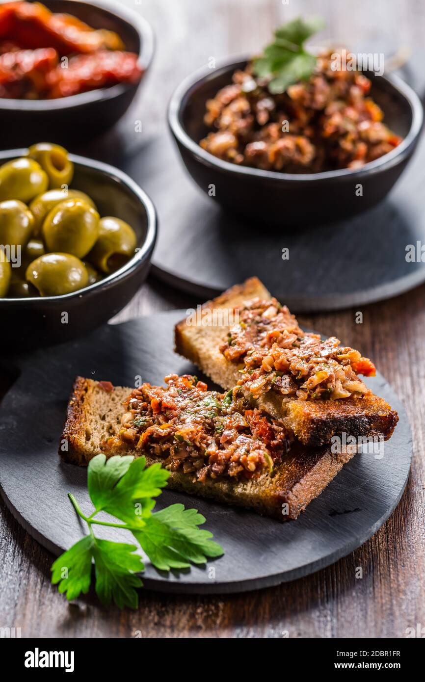 Crostini croccanti con tapenade e ingredienti. Tapenade - deliziosa pasta d'oliva francese. Foto Stock
