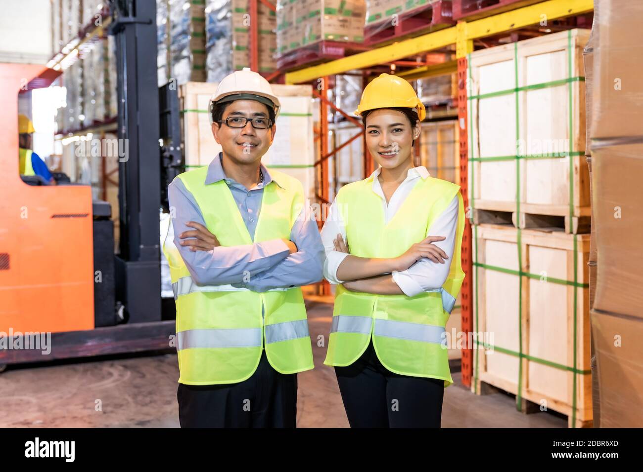 Ritratto del responsabile magazzino asiatico e braccio di lavoro attraversato con il lavoratore di magazzino azionare carrello elevatore a forche per controllare l'inventario in background. Riapertura dell'azienda Foto Stock