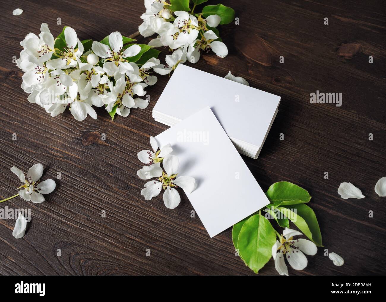 Foto di biglietti da visita bianchi e fiori su sfondo di legno. Modello per ID. Foto Stock