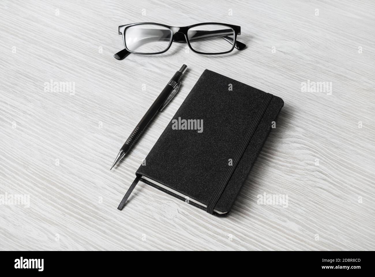 Foto di blocco note nero chiuso, bicchieri e matita meccanica su sfondo tavolo in legno chiaro. Modello per posizionare il progetto. Foto Stock