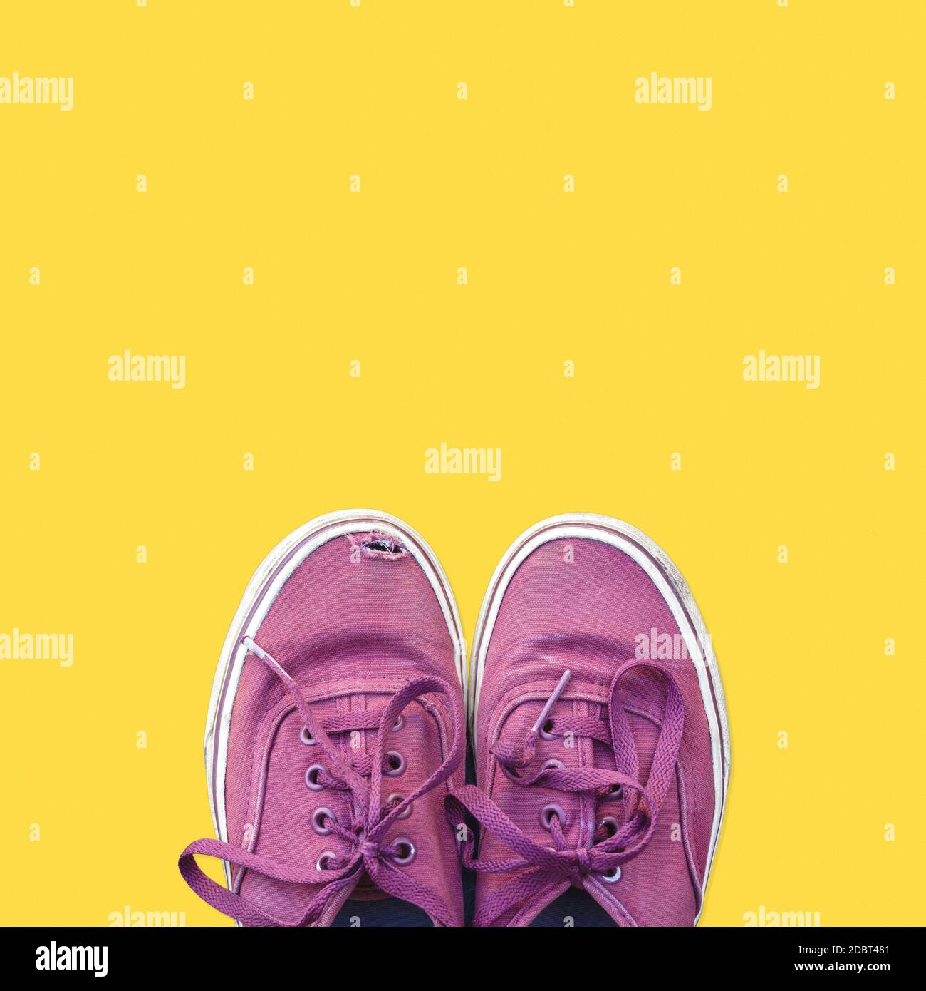 Coppia di vecchie sneaker intemperie isolate su sfondo giallo. Vista dall'alto scarpe usurate con spazio per la copia Foto Stock