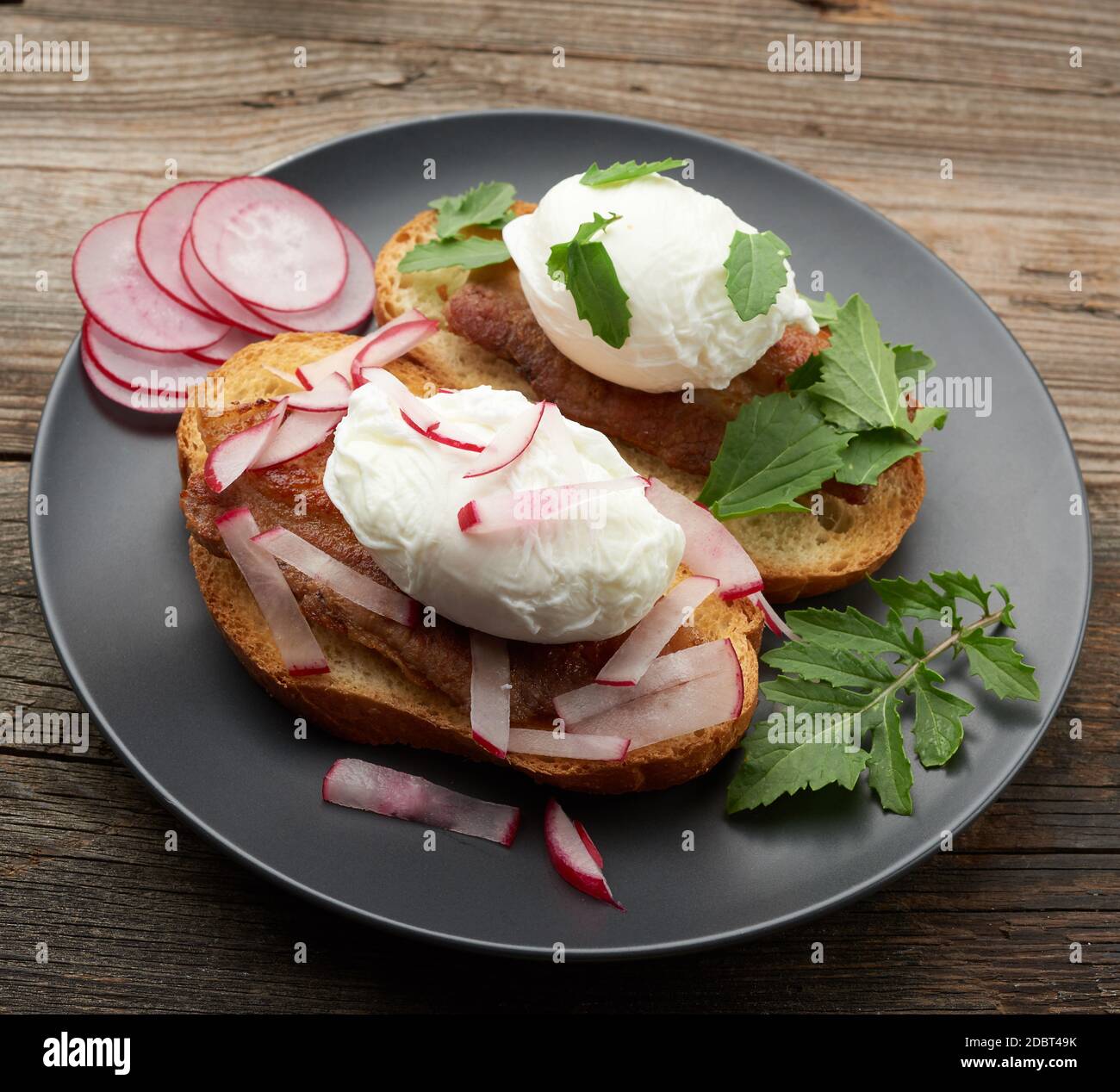 due panini su una fetta bianca di pane tostato con uova in camicia, foglie verdi di rucola e ravanello in un piatto rotondo, vista dall'alto Foto Stock