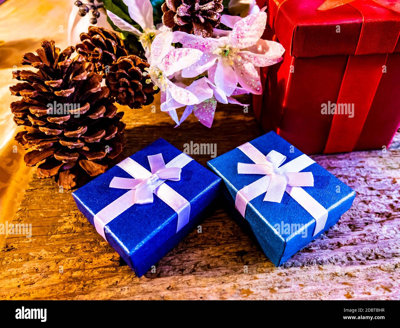 Un Natale ancora vita di colori avvolti piccoli doni con nastri bianchi e grandi coni di pino su un tavolo Foto Stock