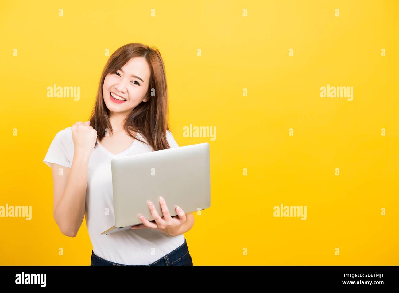 Asian Happy Portrait bella cute giovane donna teen sorriso in piedi indossare t-shirt tenere computer portatile ed eccitato celebrare il successo cercando di camer Foto Stock