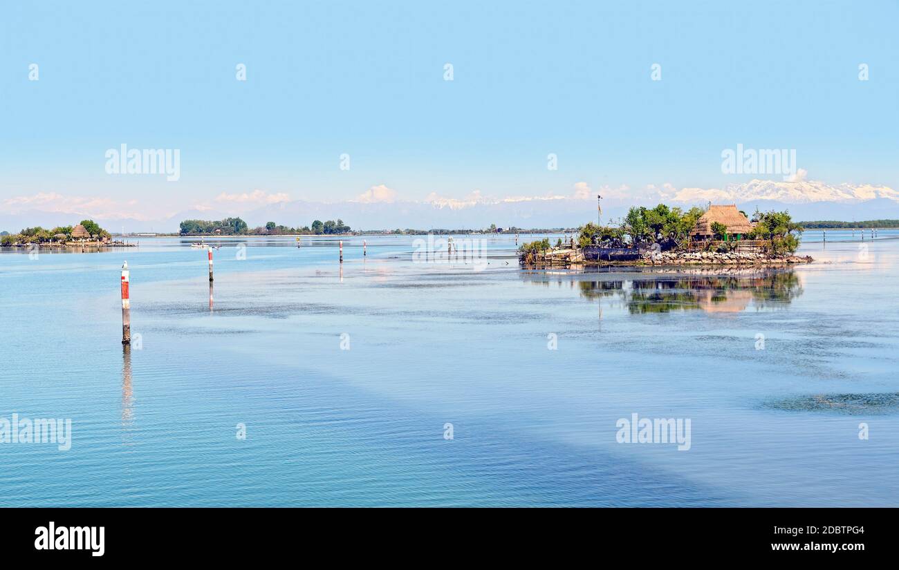 isole e canali navigabili nella laguna blu di grado con le alpi Carniche innevate sullo sfondo, Italia Foto Stock