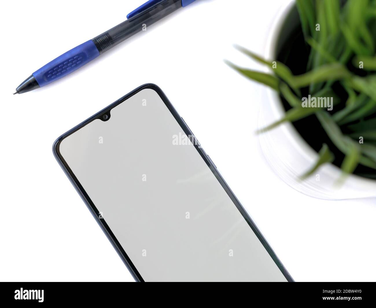 Un moderno spazio di lavoro minimalista con mockup nero per smartphone si trova sulla superficie con uno schermo vuoto. Tavolo da scrivania per ufficio con una pianta verde e un pe Foto Stock