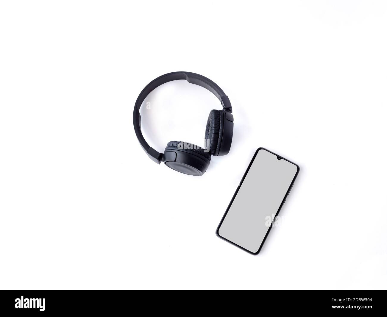 Le cuffie wireless nere e lo smartphone cellulare con un mockup a schermo vuoto si stendere sulla superficie di uno sfondo bianco. Vista dall'alto, disposizione piatta con spazio per la copia. Foto Stock