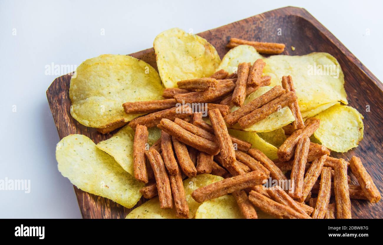 Deliziosi patatine e cracker di pane di segale salato su un piatto di legno scuro, su sfondo bianco. Spuntino ad alta caloria. Foto Stock