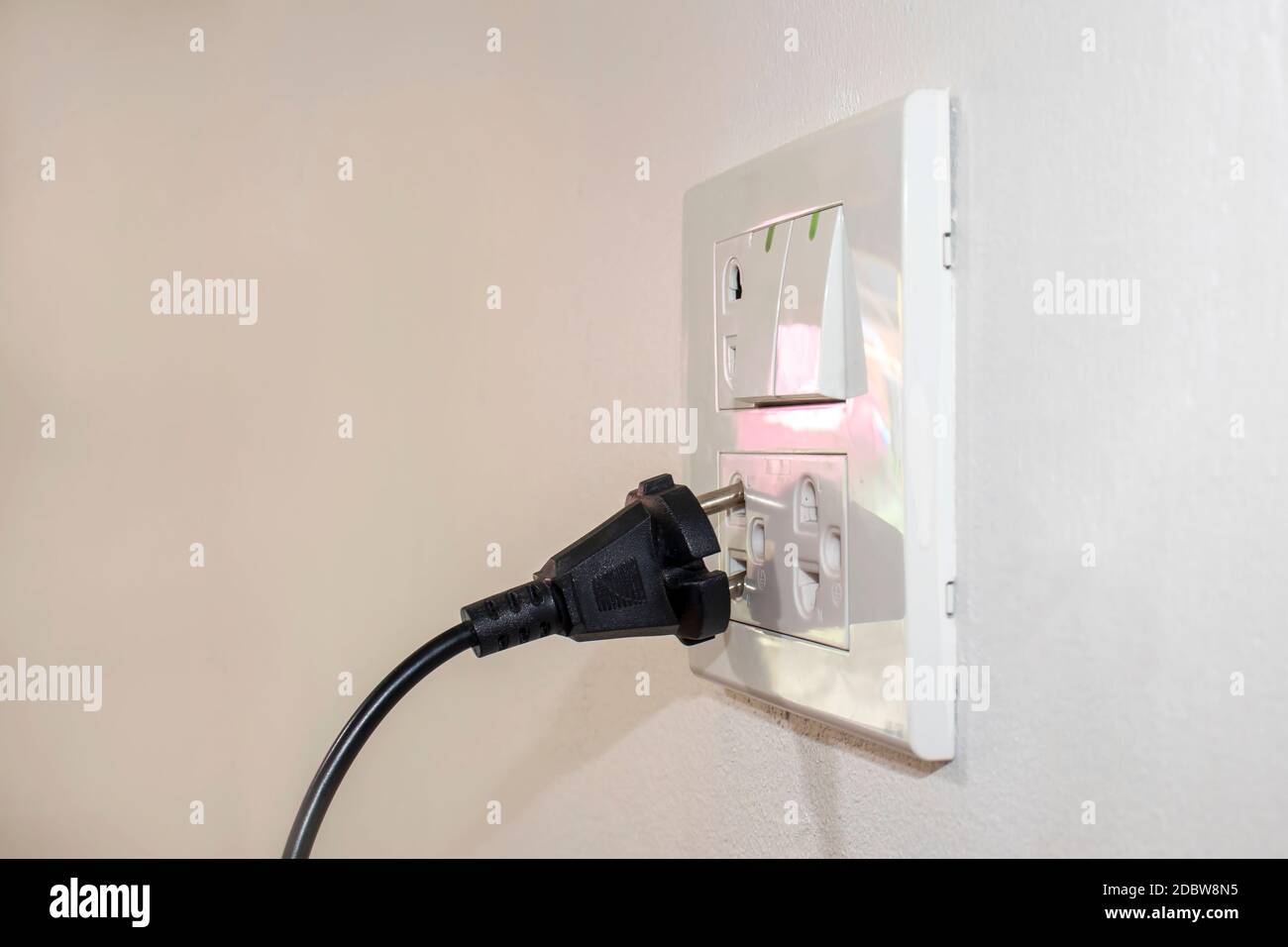 I pericoli derivanti dall'utilizzo di elettricità in casa o in ufficio includono una spina nera che non è completamente collegata alla parete bianca. Foto Stock