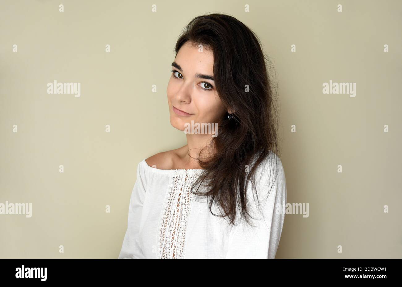 Ritratto di giovane bruna russa da 25 anni con capelli lunghi. In bianco, aprire la parte superiore della spalla e guardare nella fotocamera su sfondo grigio chiaro. Foto Stock Ritratto di giovane bruna russa da 25 anni con capelli lunghi. In bianco, aprire la parte superiore della spalla e guardare nella fotocamera su sfondo grigio chiaro. Foto Stock
