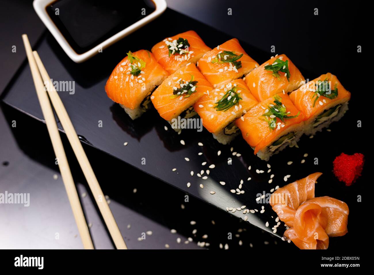 Sushi con salmone. Salsa di soia, zenzero, caviale rosso. Sushi su sfondo nero. Molti ruoli con il pesce rosso. Foto Stock