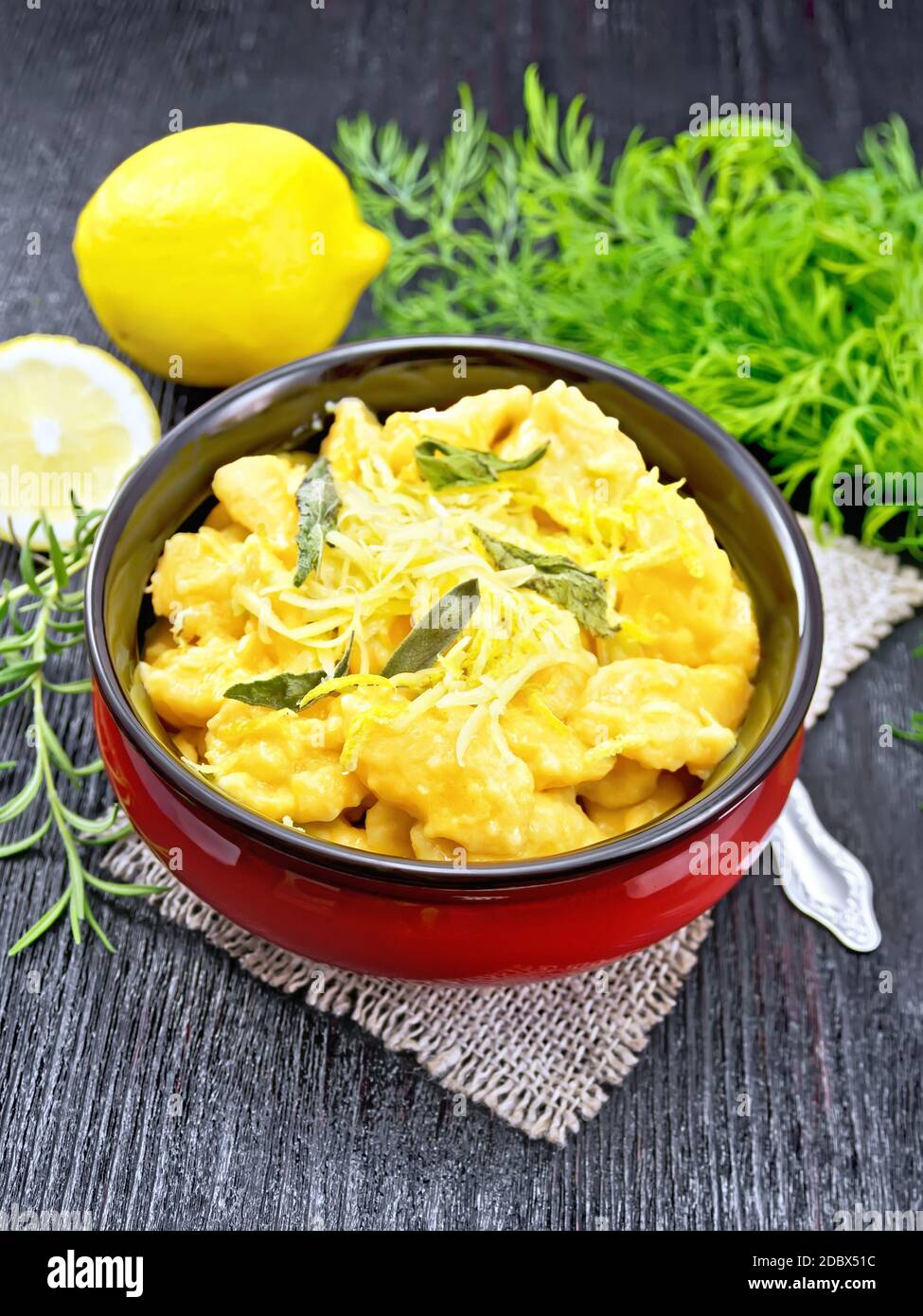 Gnocchi di zucca con salvia, limone, formaggio e burro in una ciotola su tela contro tavola di legno scuro Foto Stock