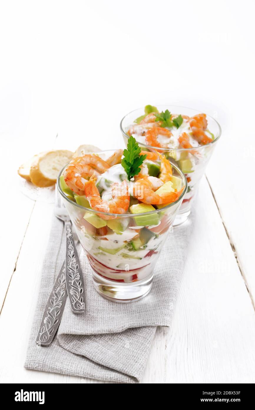 Pasta con insalata di gamberetti, avocado, Fresco cetriolo e peperone e pomodoro condito con salsa di yogurt in due bicchieri di vetro su un asciugamano, pane e delle forcelle Foto Stock