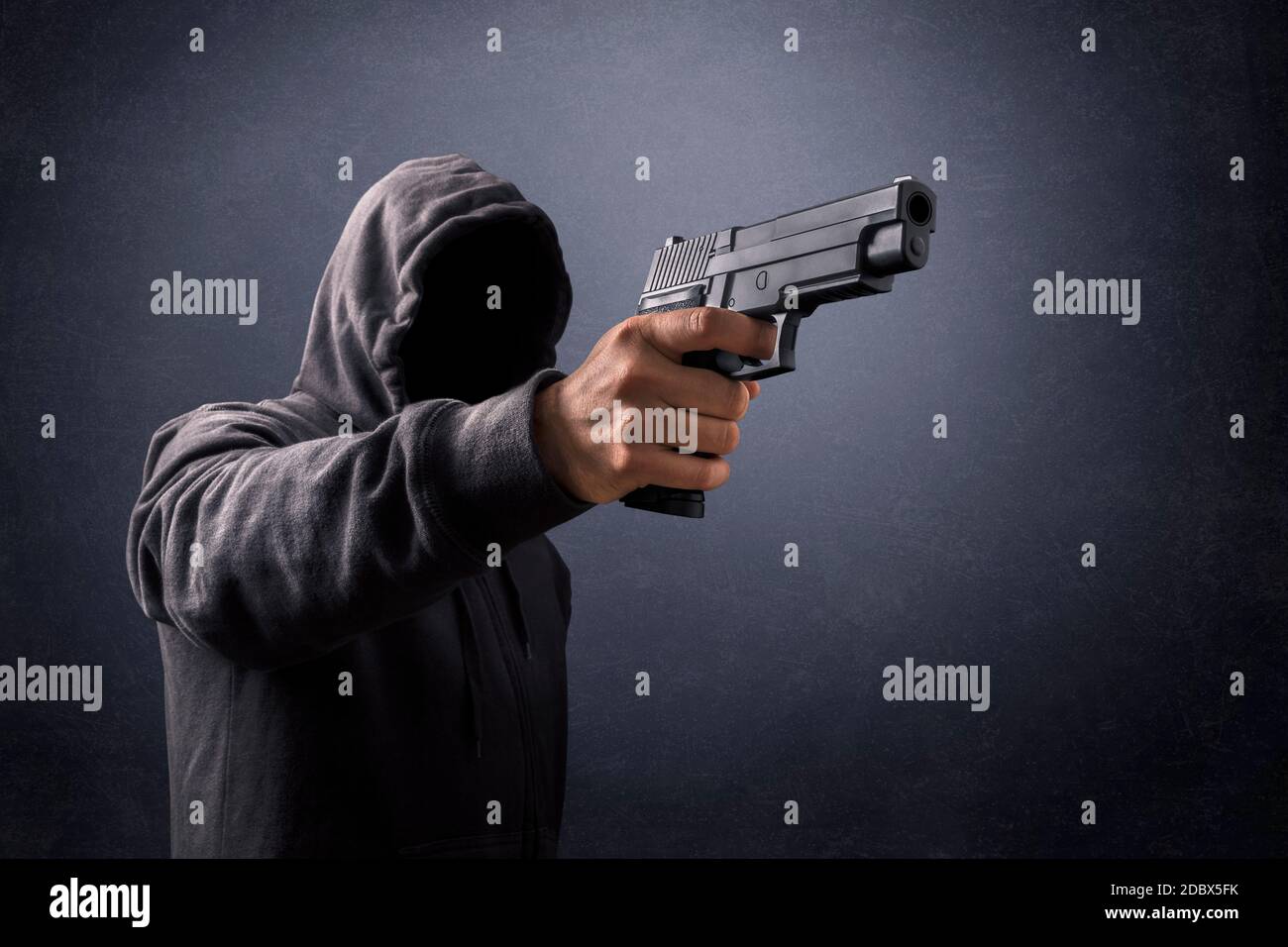 Uomo incappucciato con una pistola nel buio Foto Stock