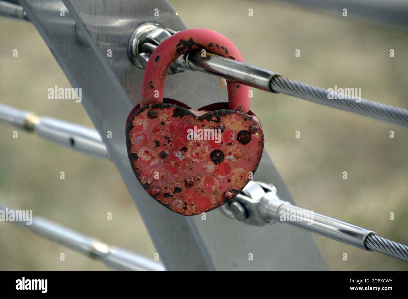 Vecchio lucchetto rosso arrugginito a forma di cuore appeso su una recinzione in metallo all'aperto Foto Stock