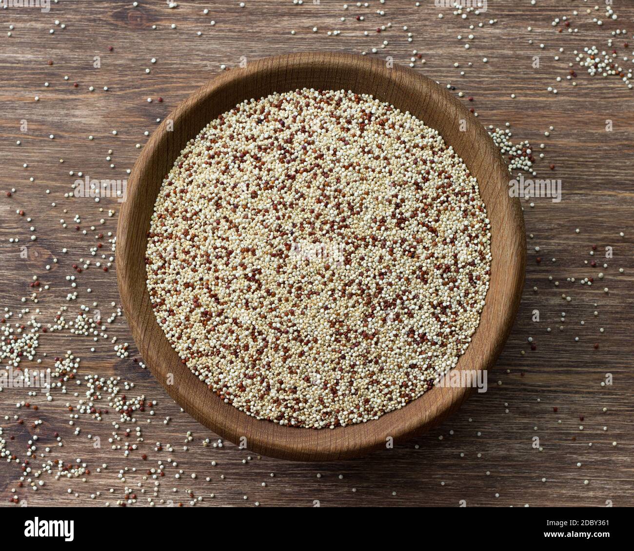 Quinoa crude mescolate in ciotola di legno su tavola di legno. Supercibo sano e senza glutine Foto Stock