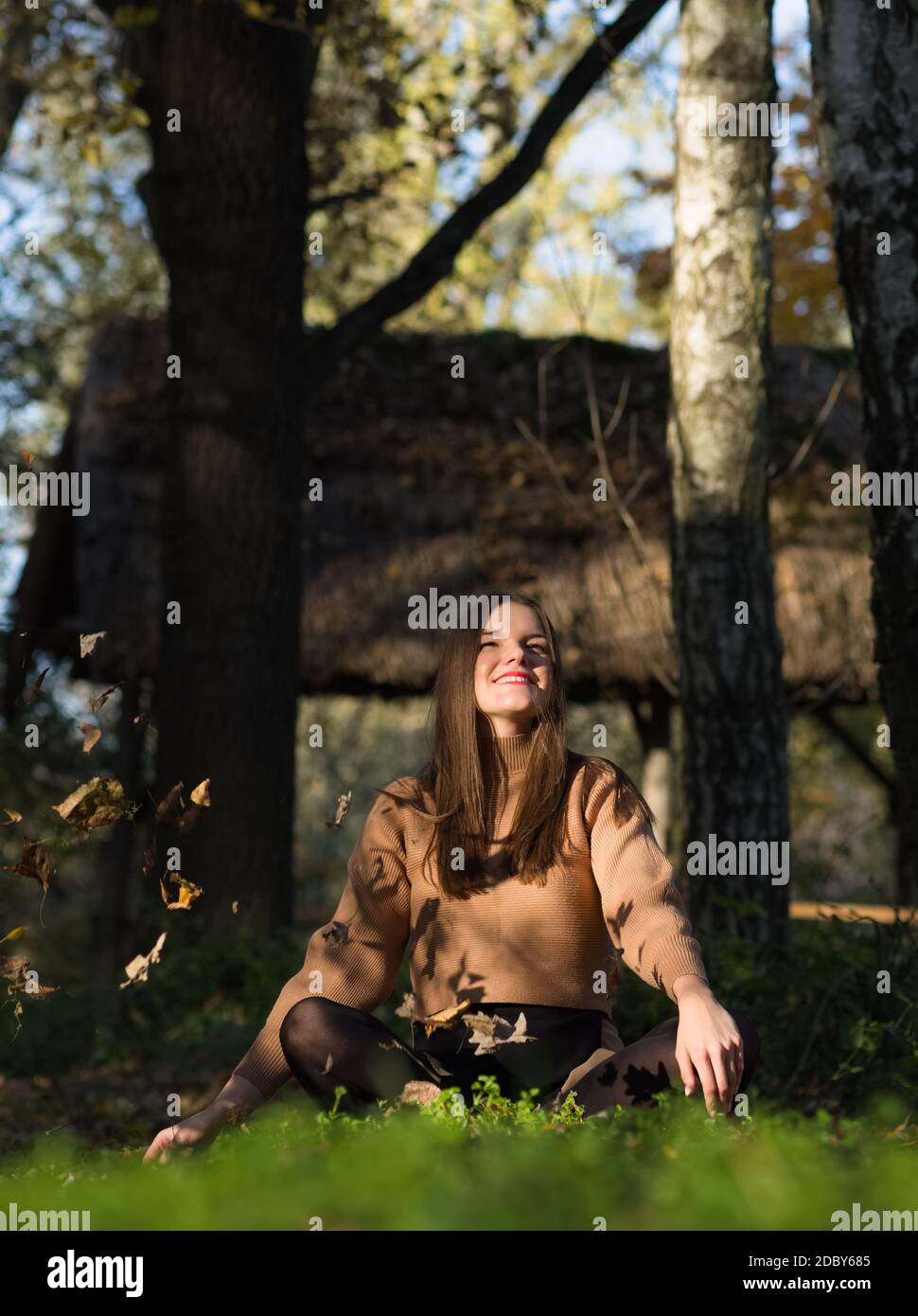 Giovane bella Brunette capelli lunghi Donna seduta nella foresta Con foglie cadenti Foto Stock