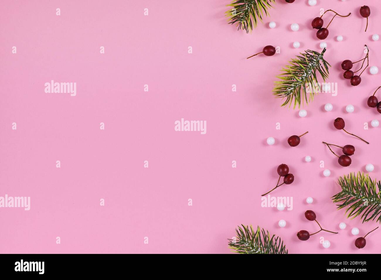 Bacche invernali rosse di stagione, palle di neve bianche e rami di abete sul lato di sfondo rosa chiaro con spazio di copia vuoto Foto Stock
