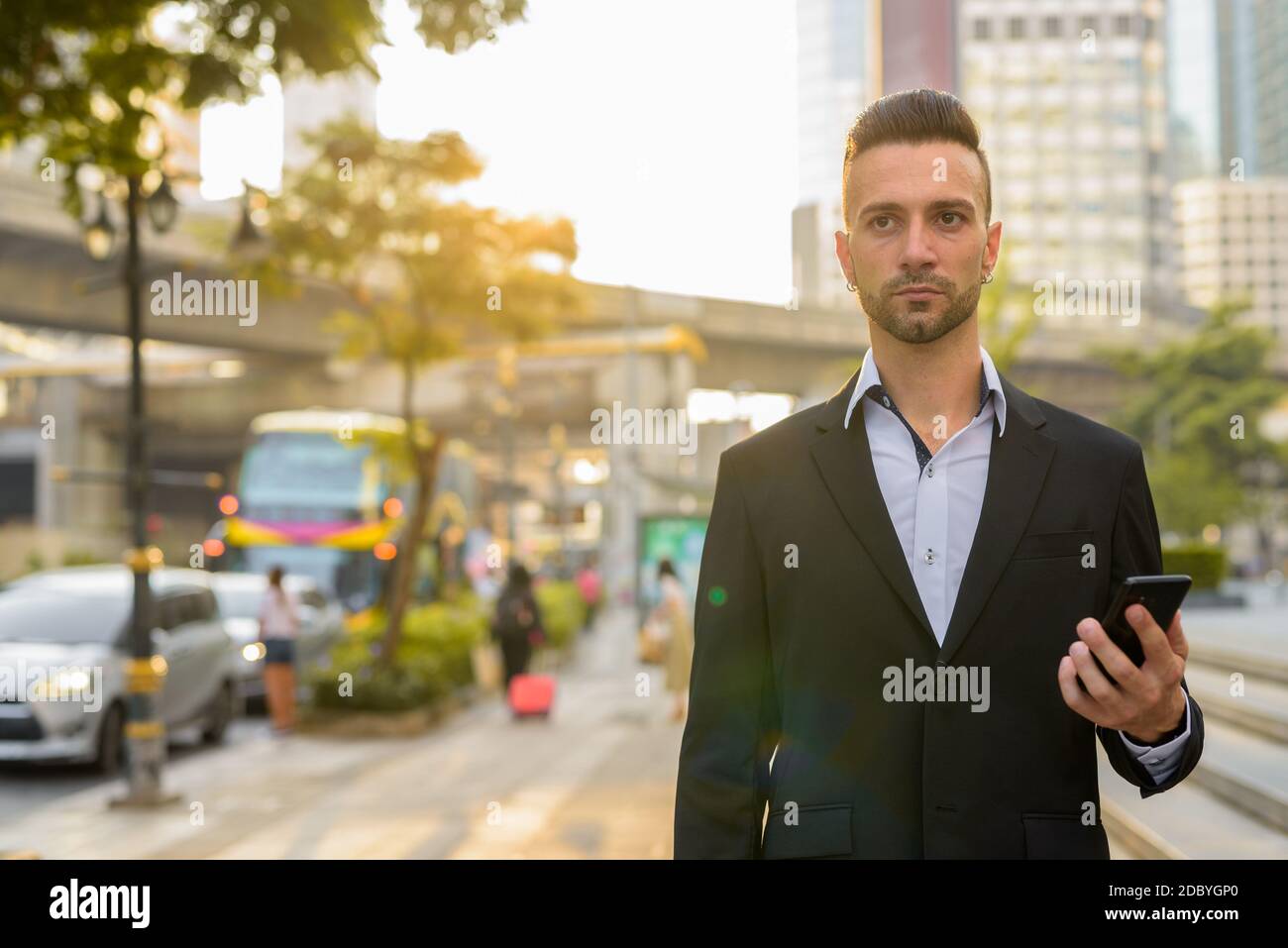 Uomo d'affari in città in attesa di taxi mentre si utilizza l'app mobile con telefono Foto Stock