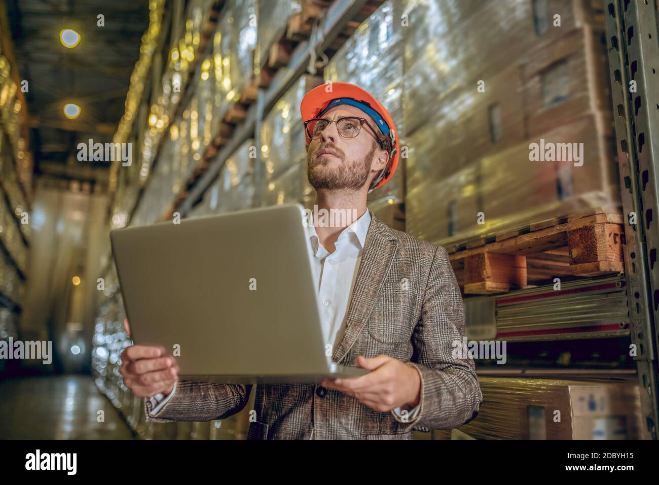 Responsabile del magazzino in casco arancione che tiene un computer portatile e ispeziona un magazzino Foto Stock