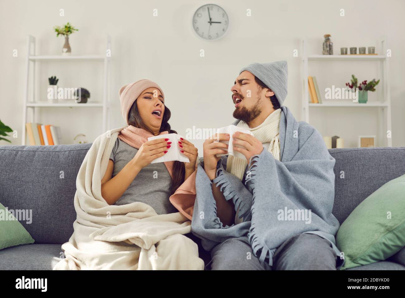 Giovane coppia avvolta in coperte calde seduta sul divano e. starnuti in  fazzoletti di carta Foto stock - Alamy