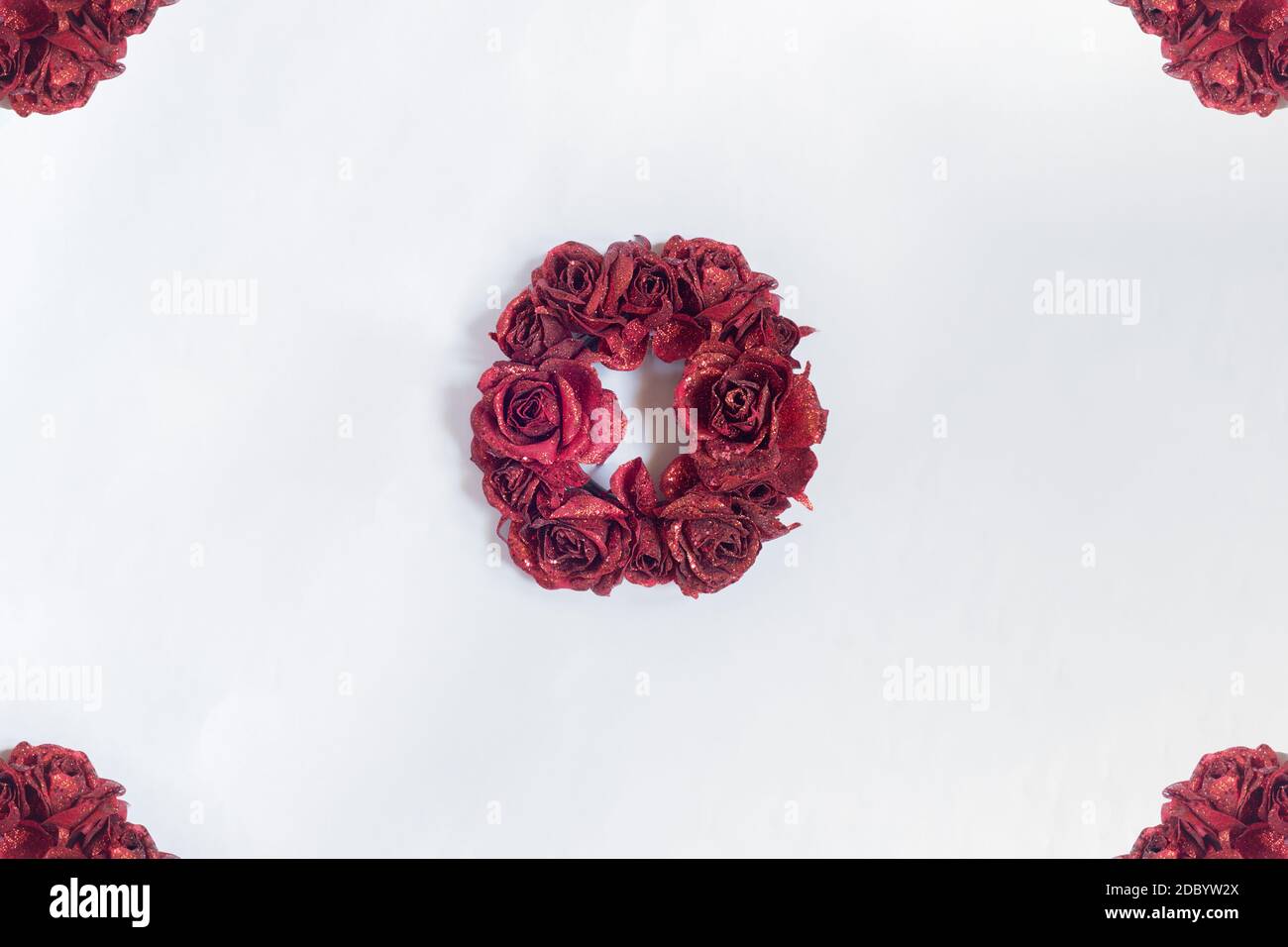 Una cornice di rose rosse con una corona di Natale decorativa al centro e sfondo bianco. Tradizionale festa di Natale ornamento. Foto Stock