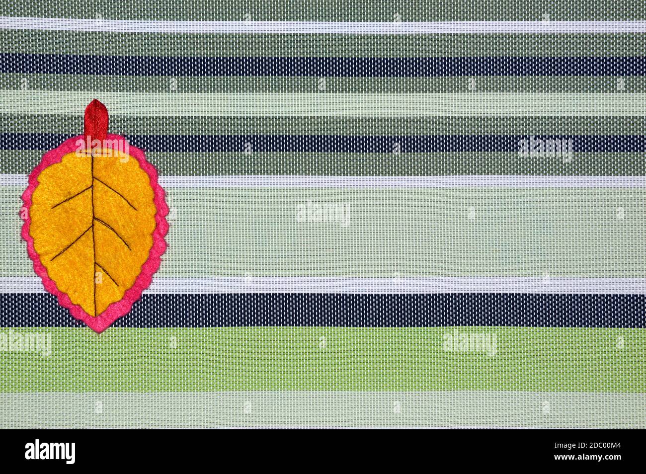 Foglia gialla fatta a mano di tessuto su sfondo a strisce con copia spazio Foto Stock