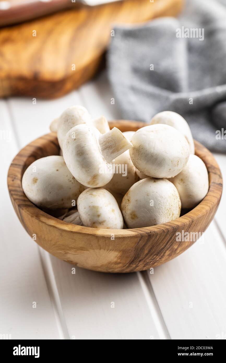 Funghi champignon bianchi freschi in ciotola di legno su tavola bianca. Foto Stock